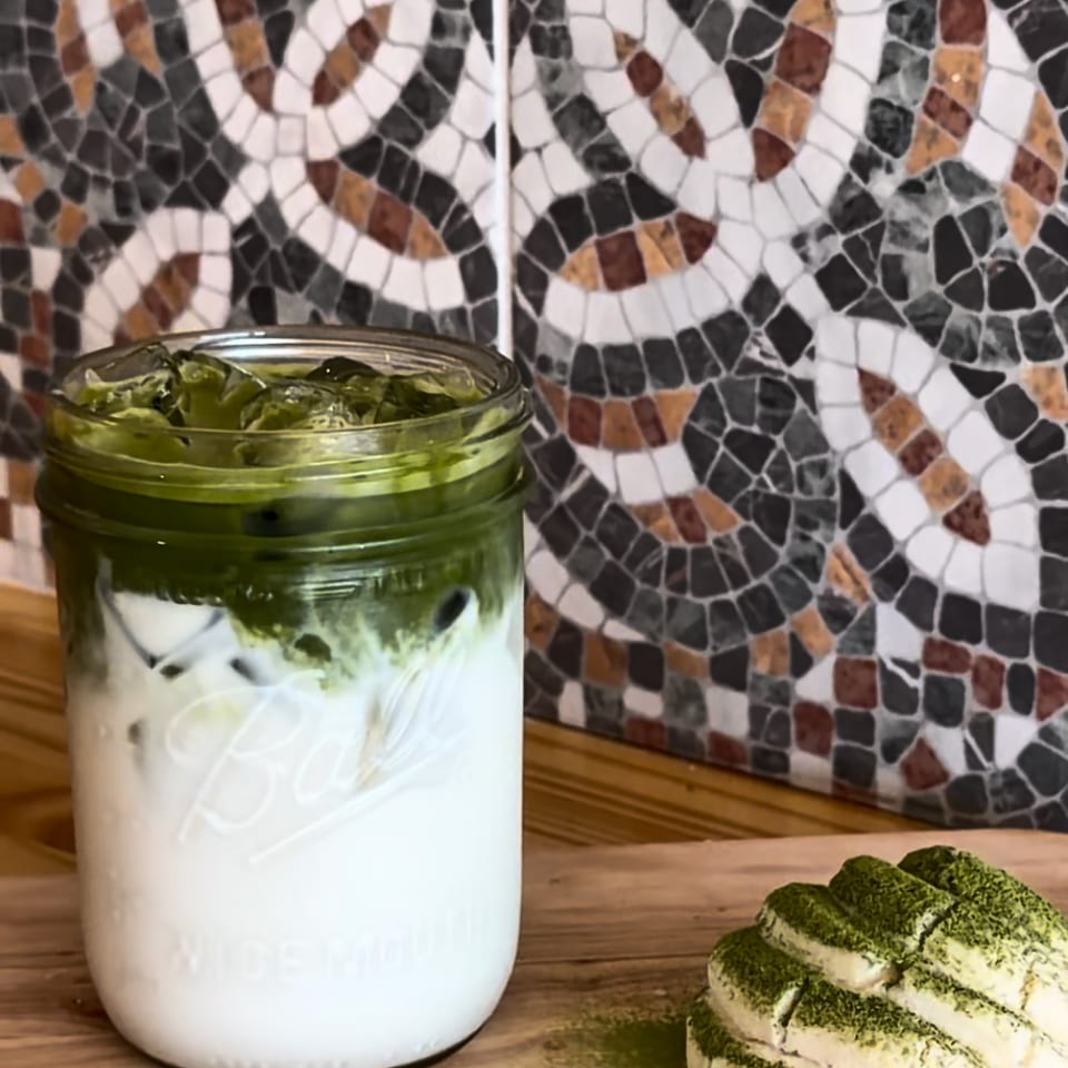 Iced matcha latte in a mason jar with a matcha-dusted pastry on a wooden board.