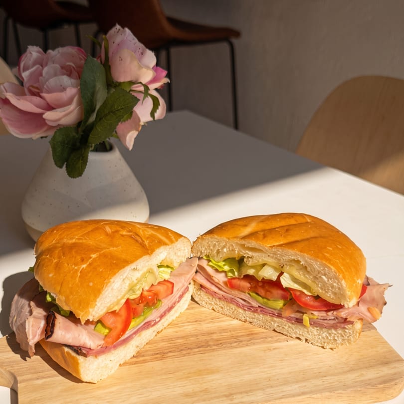 Hearty sandwich with ham, lettuce, and tomato, cut in half on a wooden board with flowers.