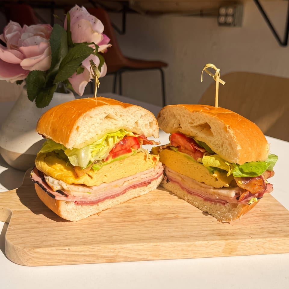 Hearty sandwich halves with egg, ham, bacon, lettuce, and tomato on a wooden board.