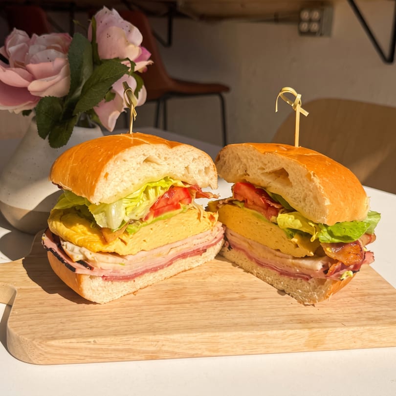Hearty sandwich halves with egg, ham, bacon, lettuce, and tomato on a wooden board.